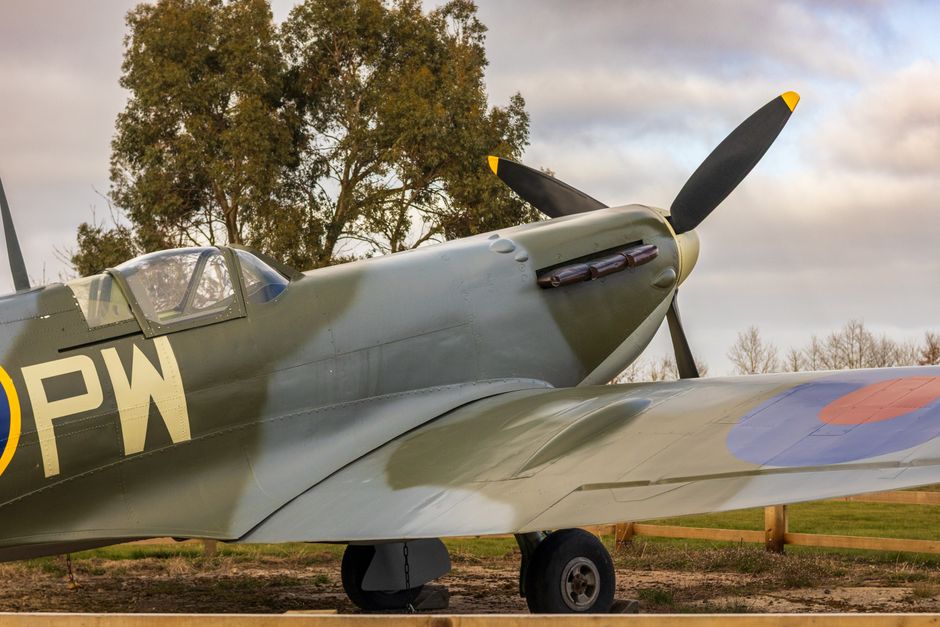 A vintage military aircraft flying in clear blue sky, featuring a dark navy blue fuselage with distinctive roundel insignia on the side. The airplane has a twin-engine configuration with propellers in
